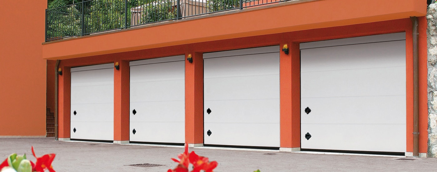 Batteria di quattro portoni sezionali TEG bianchi su edificio residenziale con facciata arancio